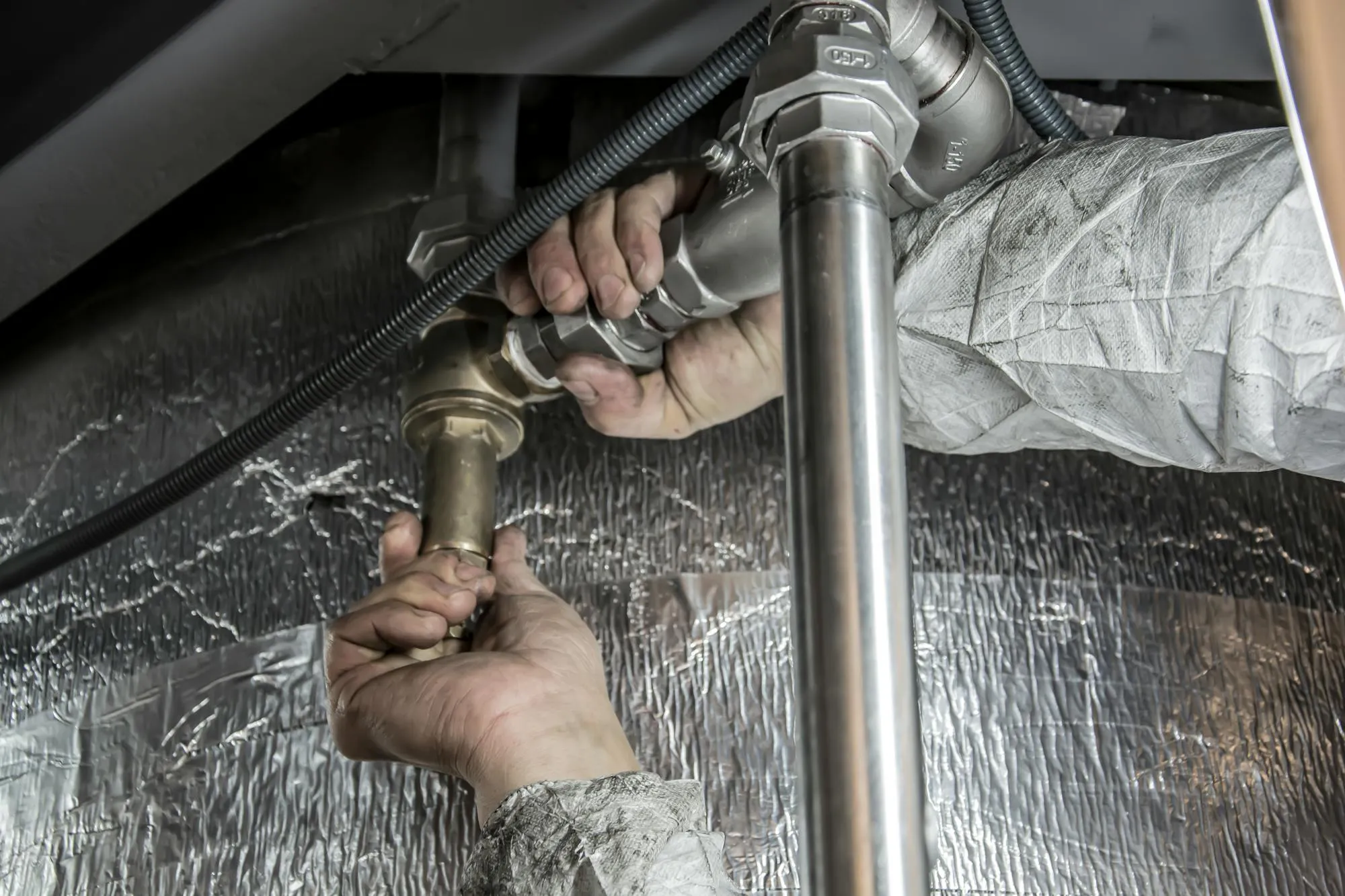 Hands tightening a brass union under a sink in a Norwich kitchen