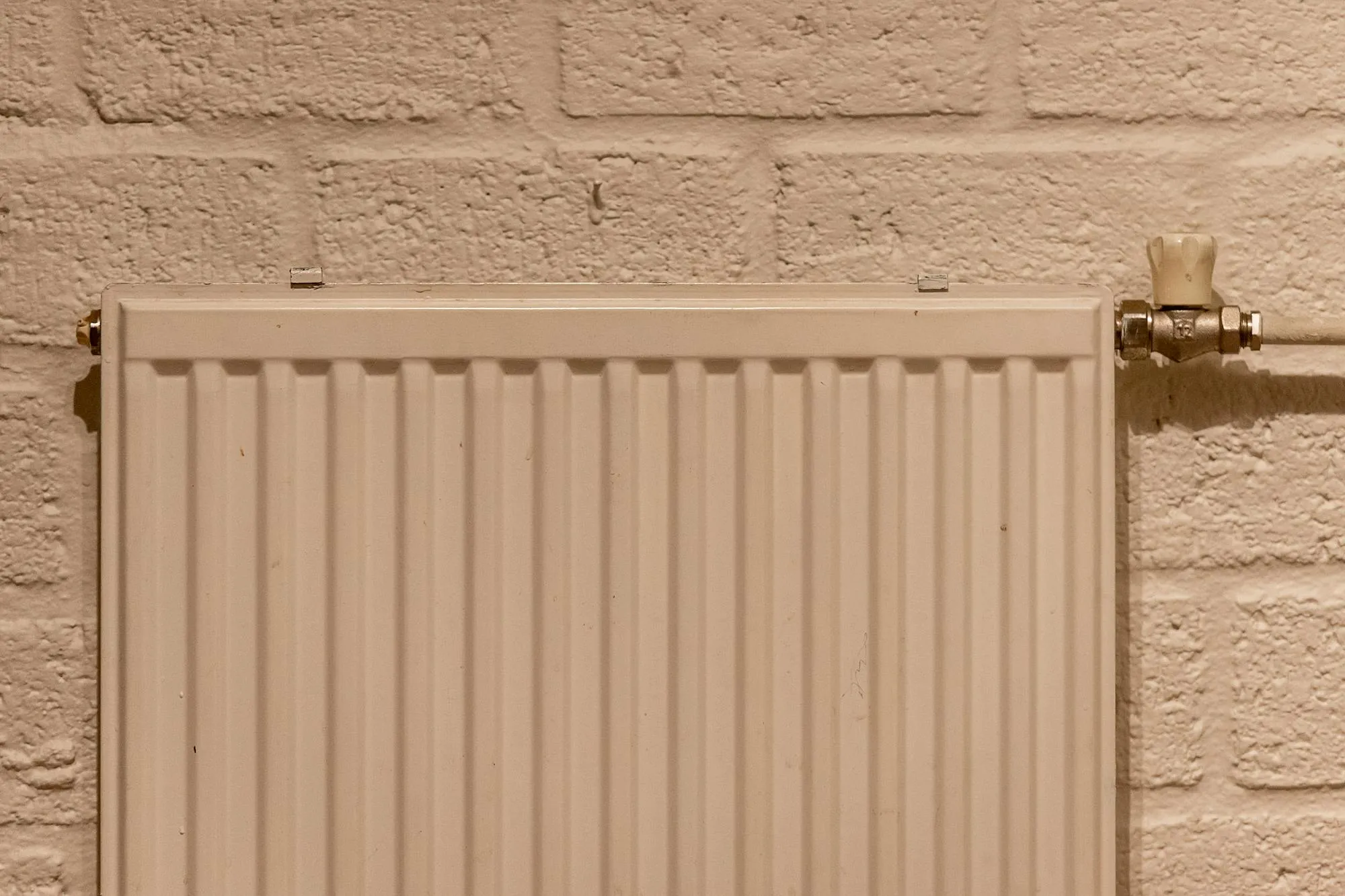 White panel radiator with a chrome thermostatic valve on a brick wall